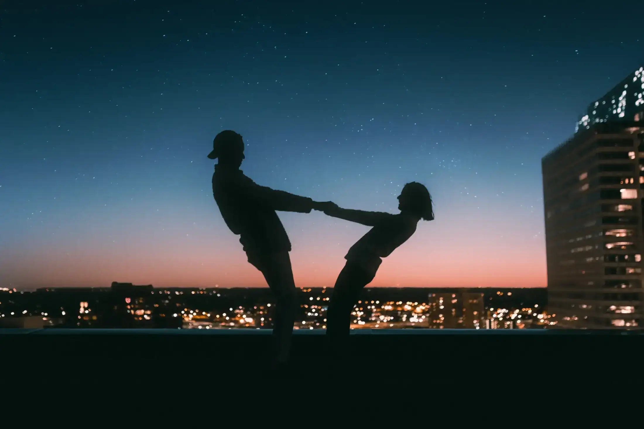 Silhouette of a couple holding hands on a starry rooftop.