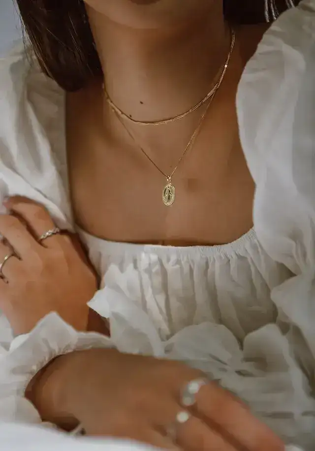 Woman wearing layered gold necklaces and a white ruffled top.