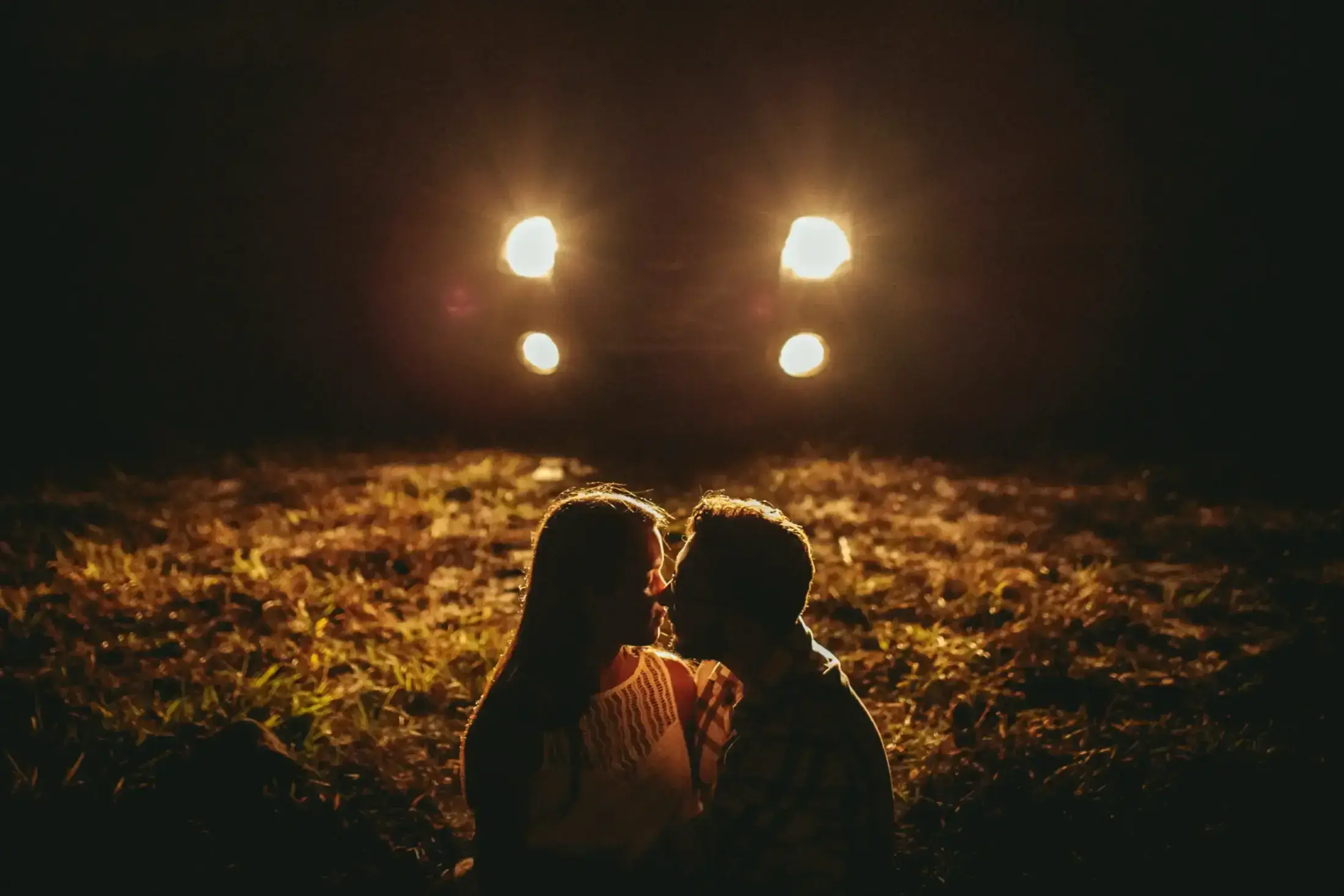 Silhouette of a couple kissing before bright car headlights.