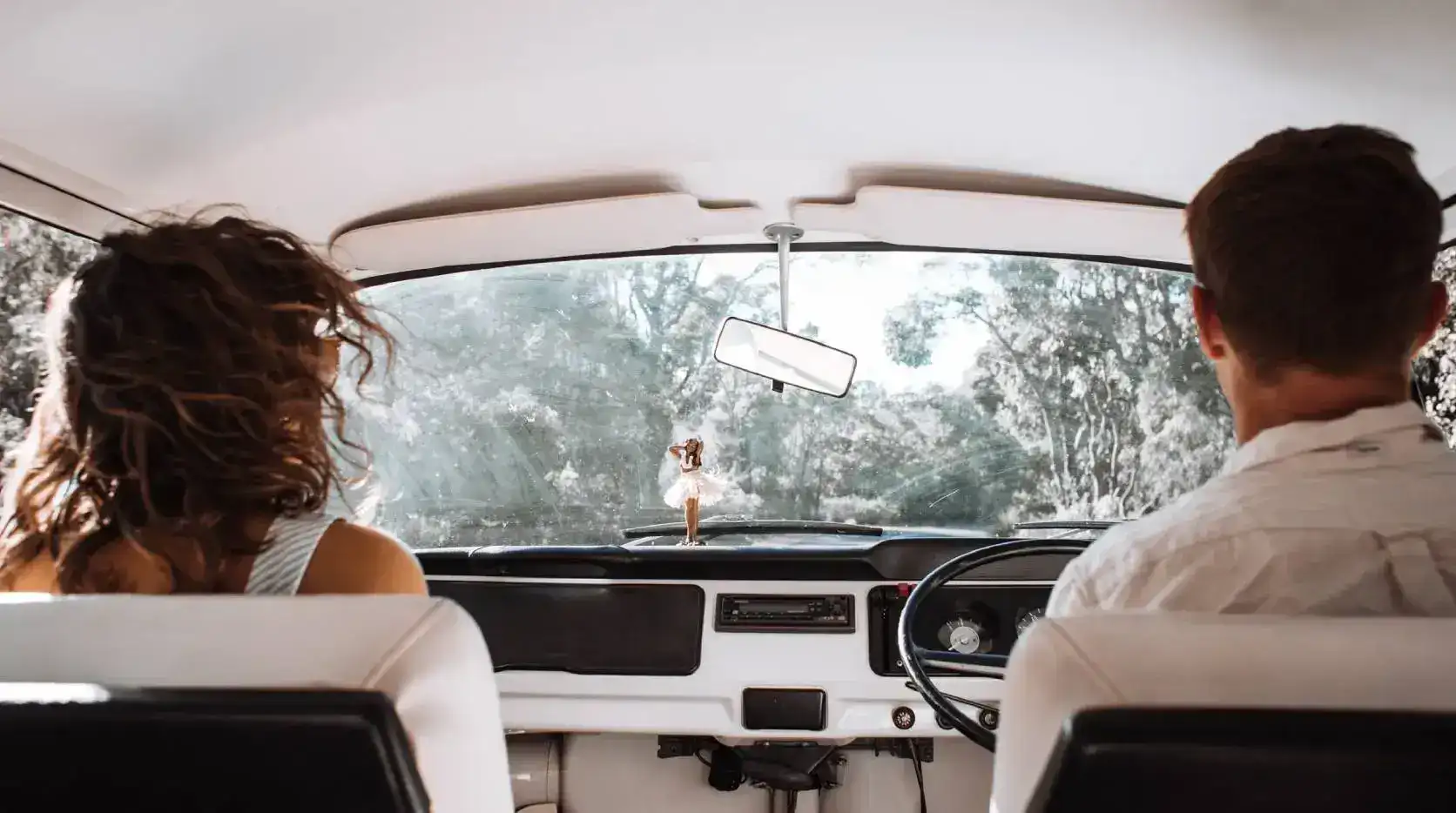 A couple driving a vintage car through a wooded area.
