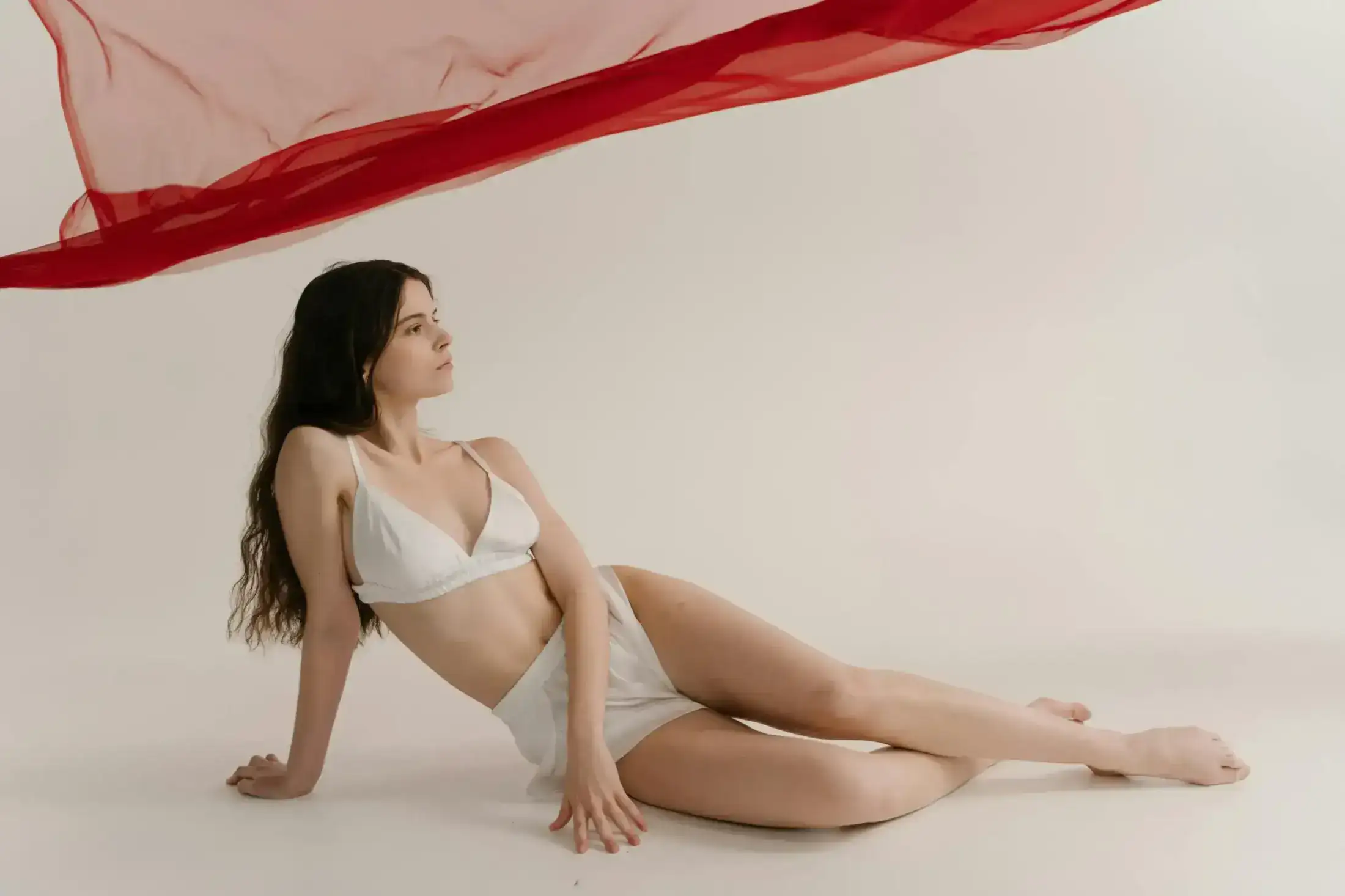Woman in white lingerie under a floating red fabric.