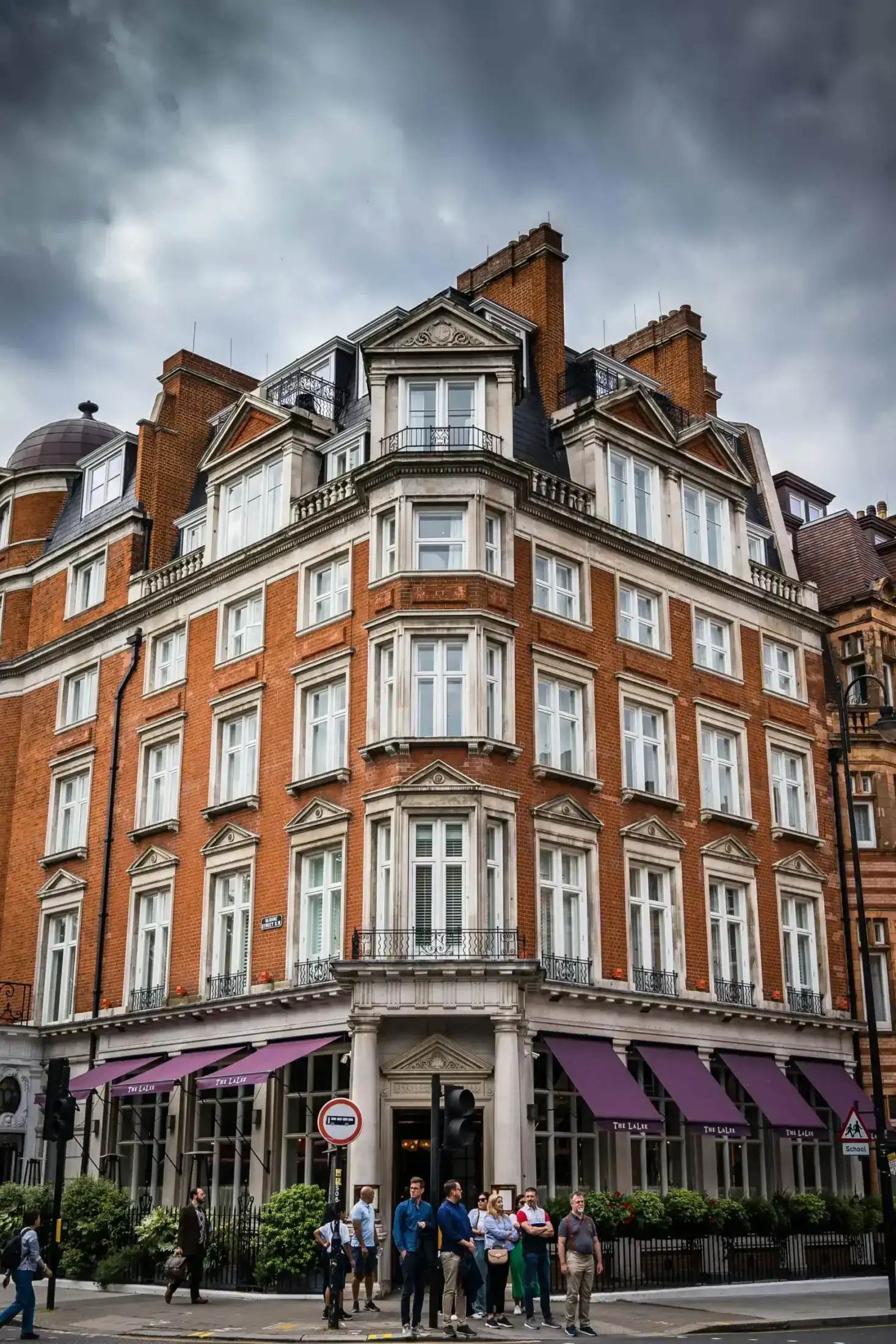 Red brick corner building with purple awnings and pedestrians.