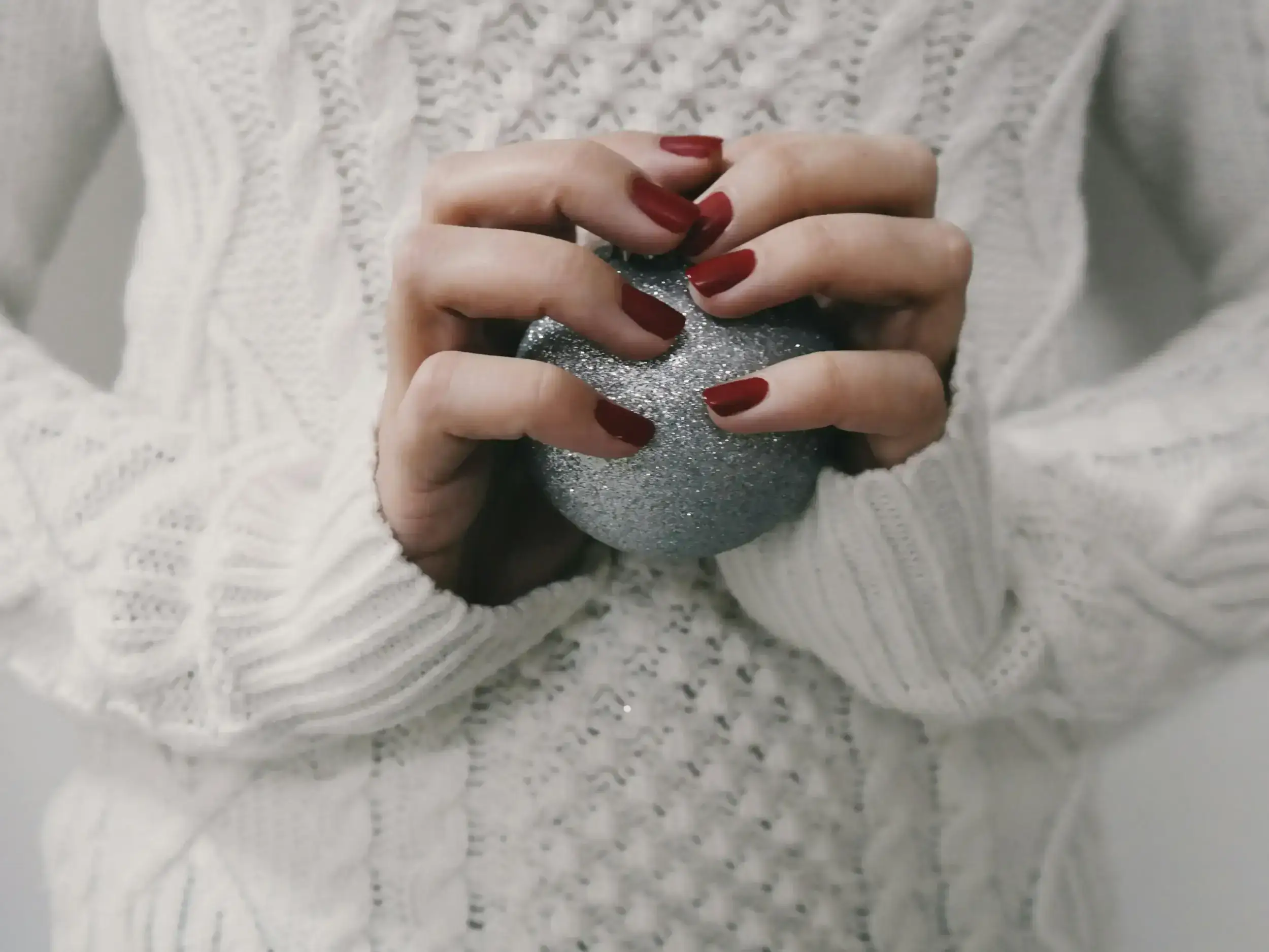 Hands with red nails holding a silver glittery bauble.