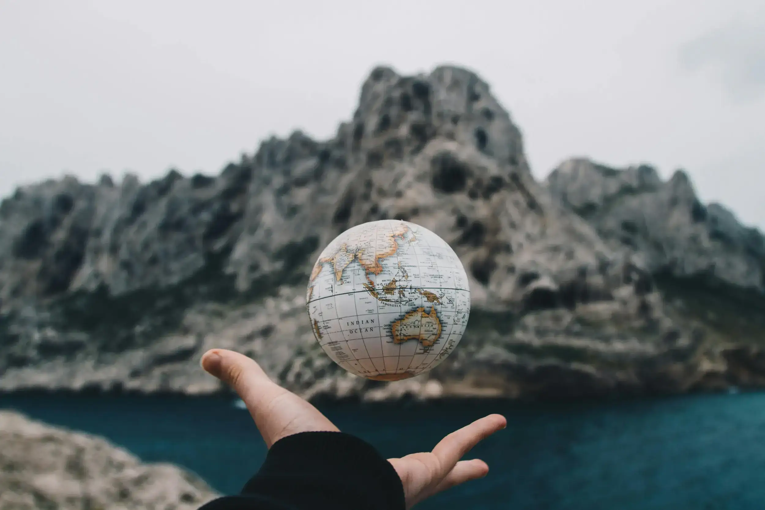 Small globe floating above a hand with mountains behind.