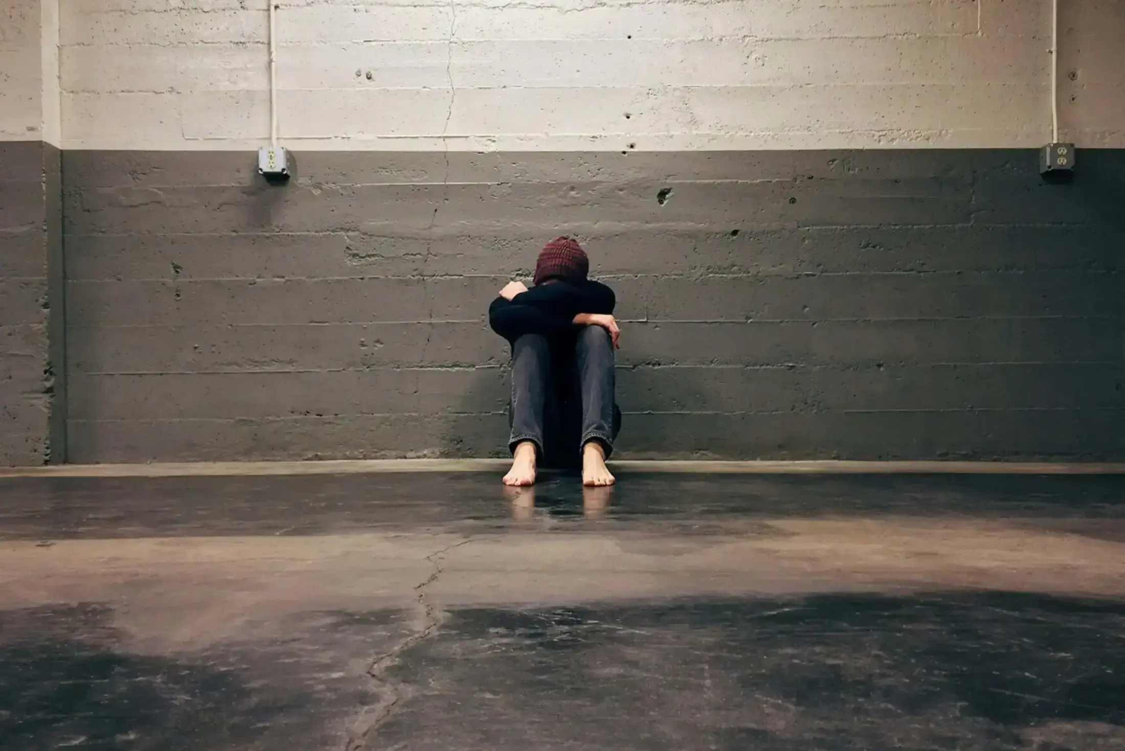 Person sitting alone with head down against a wall.