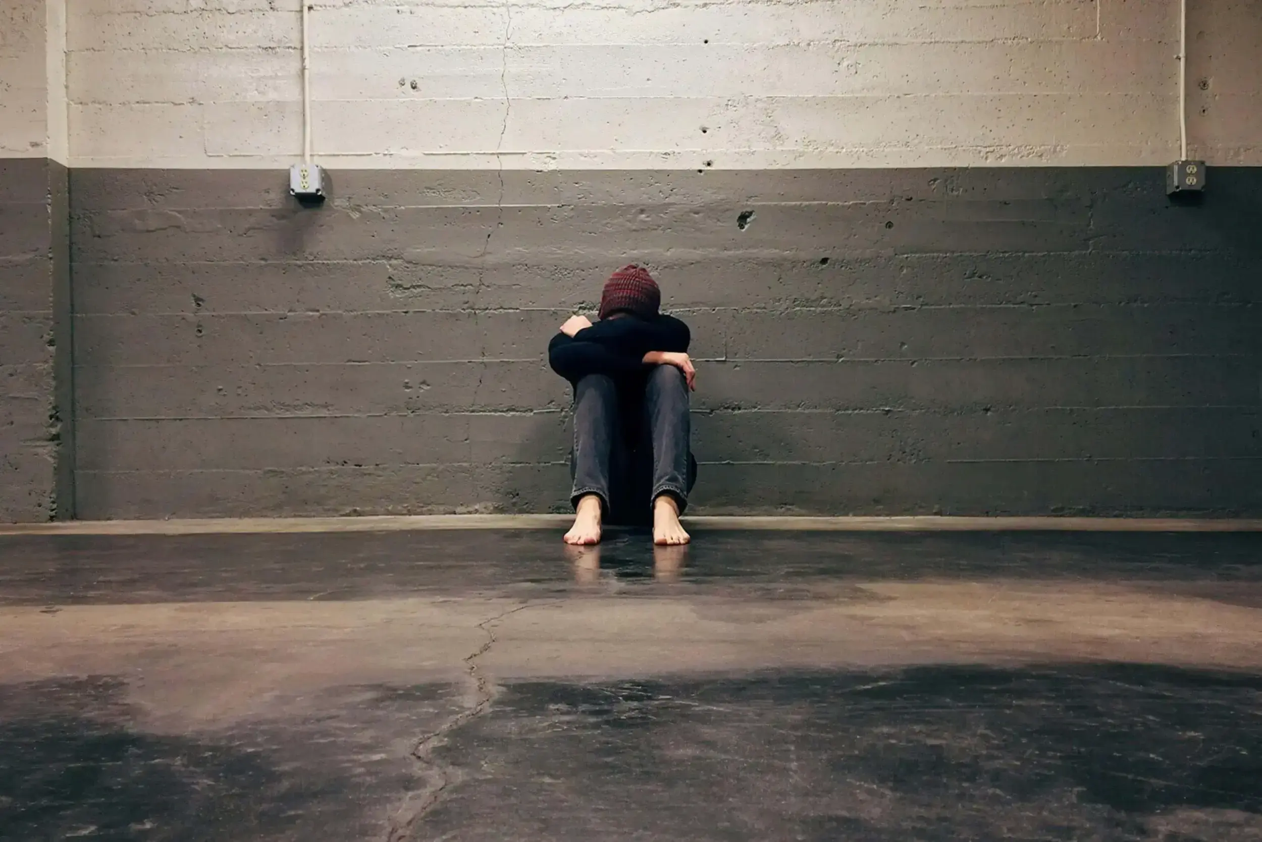 Person sitting alone with head down against a wall.