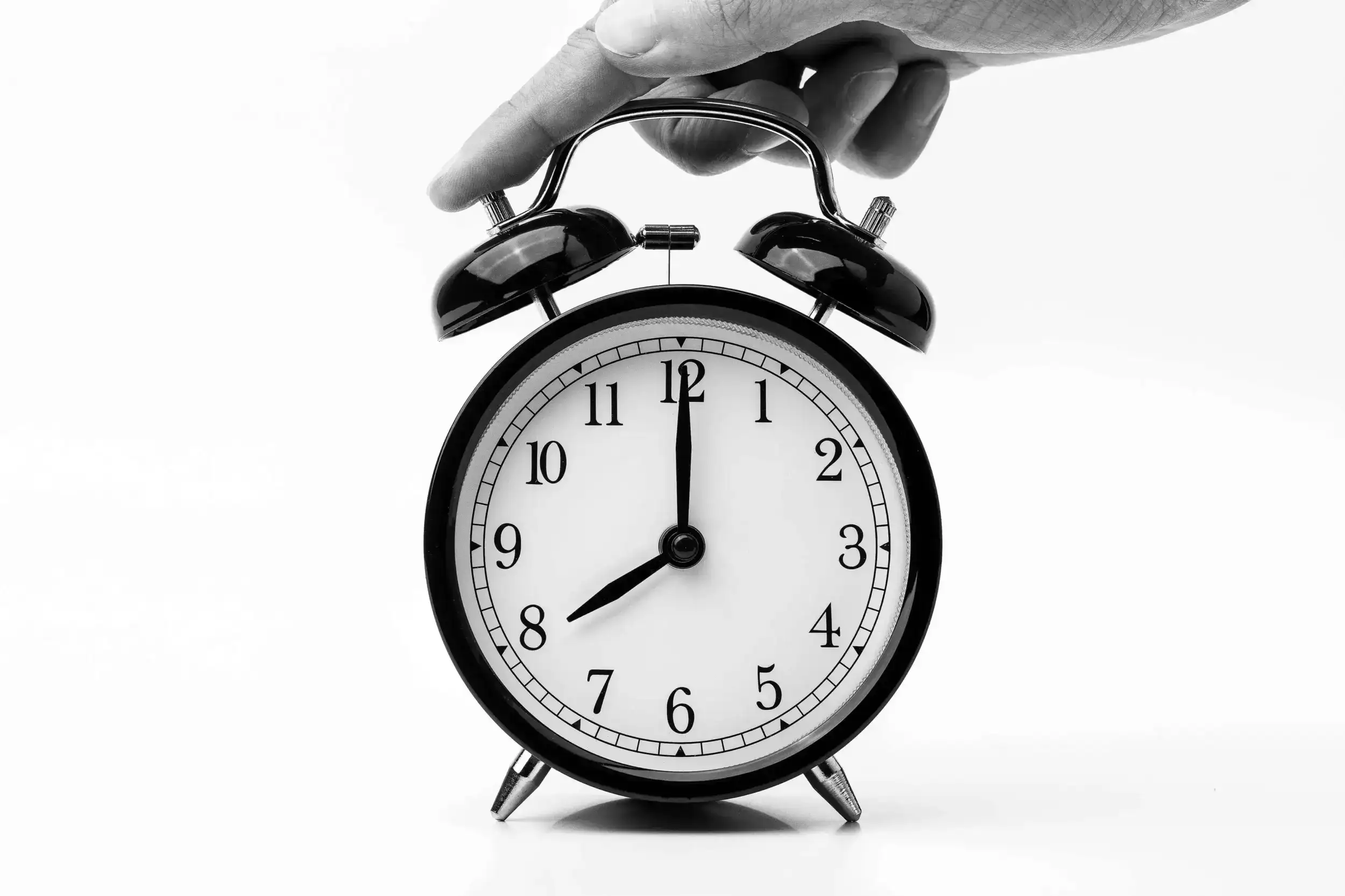 Hand reaching to stop a classic twin-bell alarm clock.