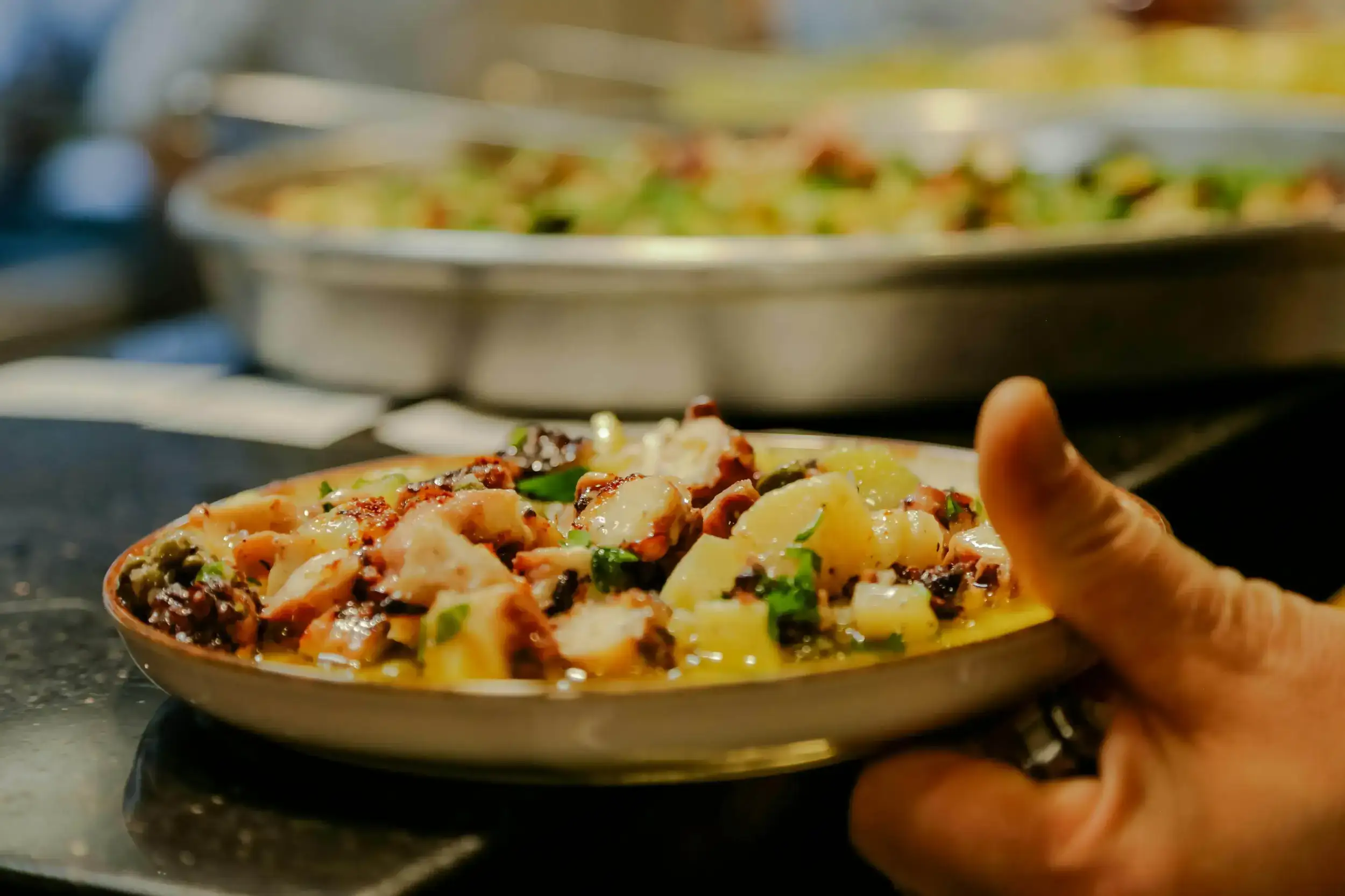 Hand holding a plate of octopus and potato salad.