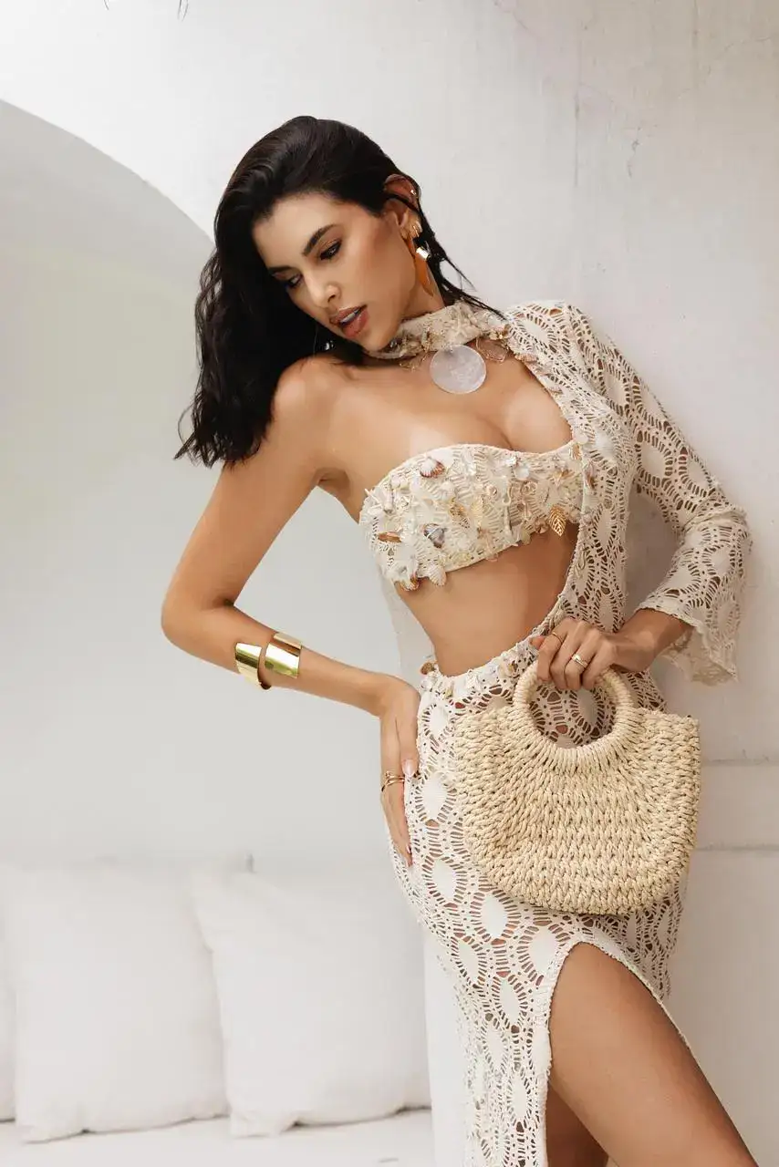 Woman in cream crochet outfit holding a straw bag.