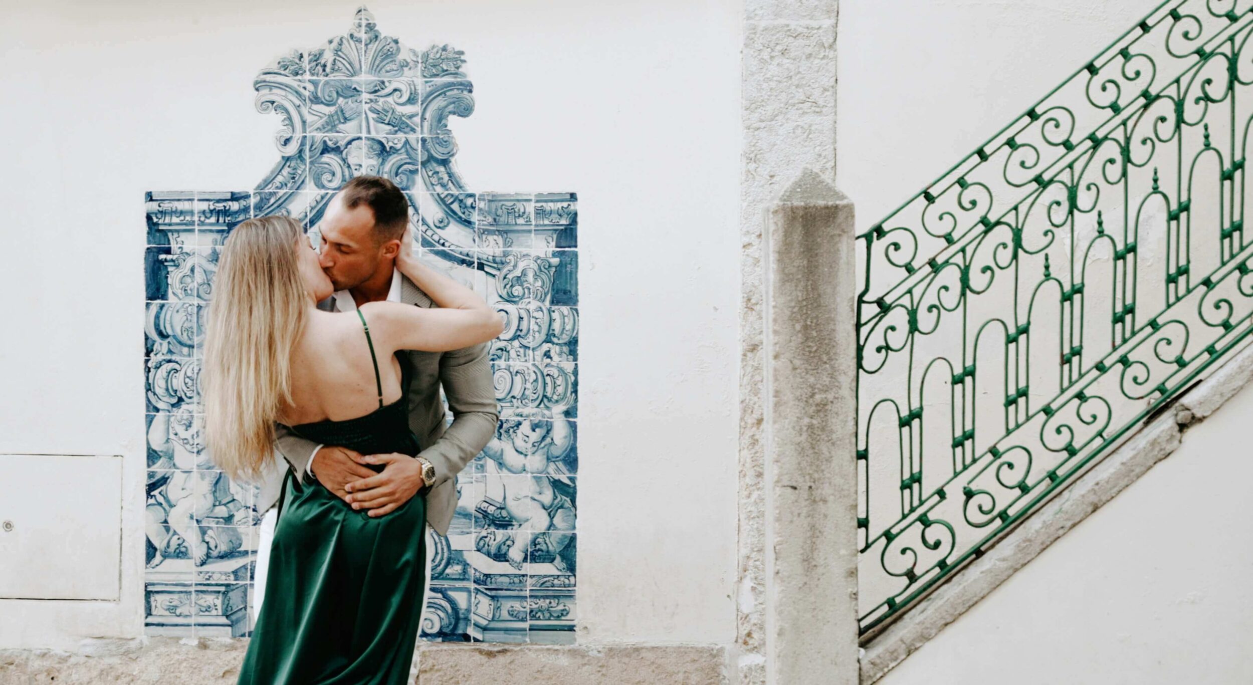 Couple kissing in front of blue decorative wall tiles.