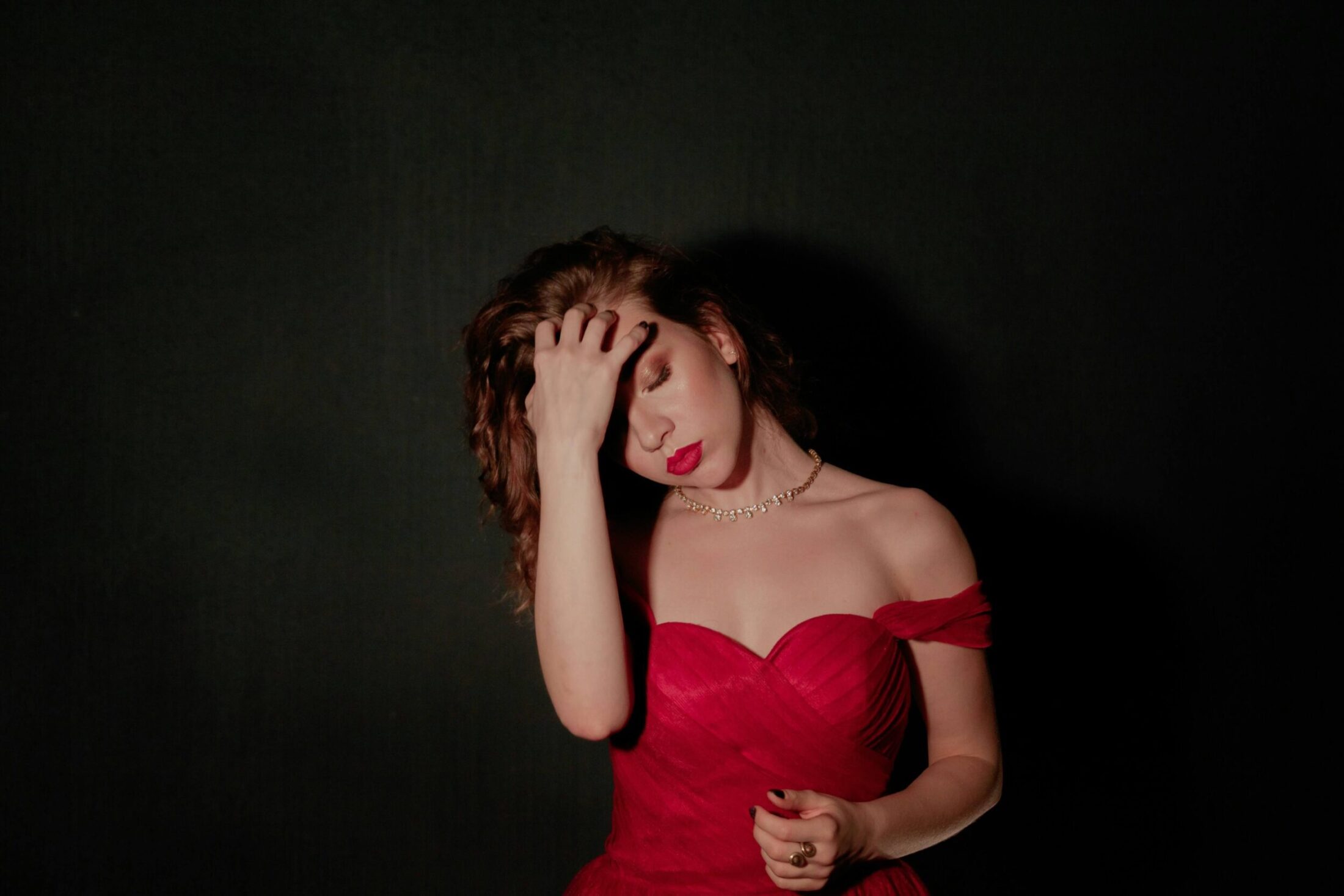 Woman in a red off-the-shoulder dress against black background.