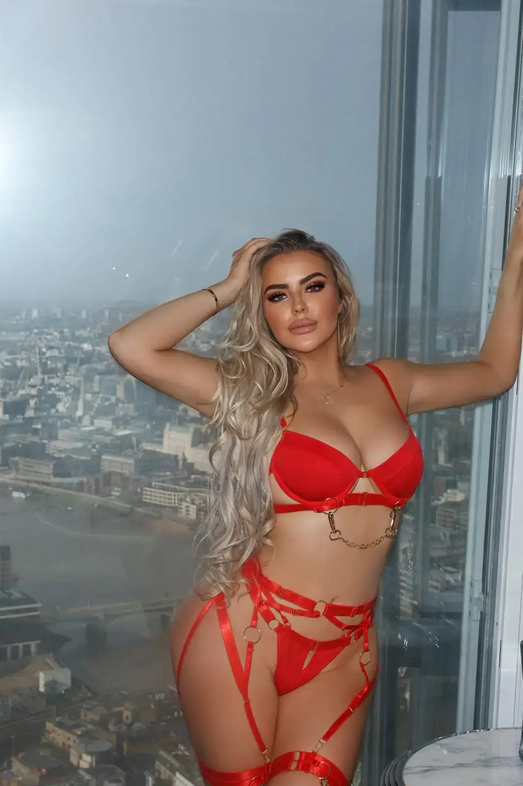 Woman in red lingerie set posing by a high-rise window.